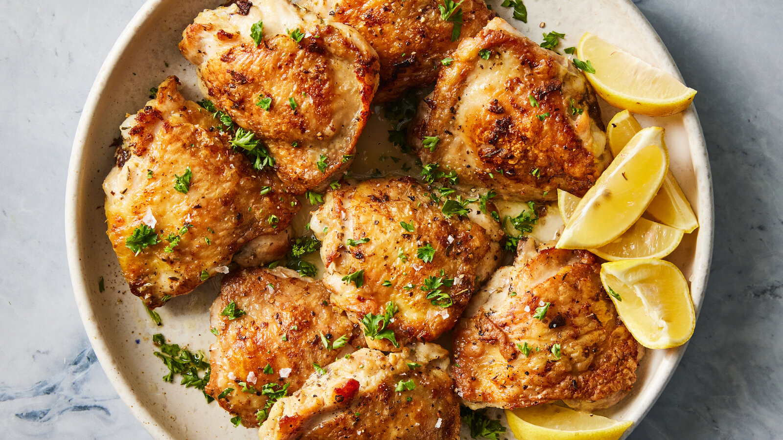 Chicken thighs in a mixing bowl being tossed with olive oil, paprika, garlic powder, and black pepper on a kitchen counter