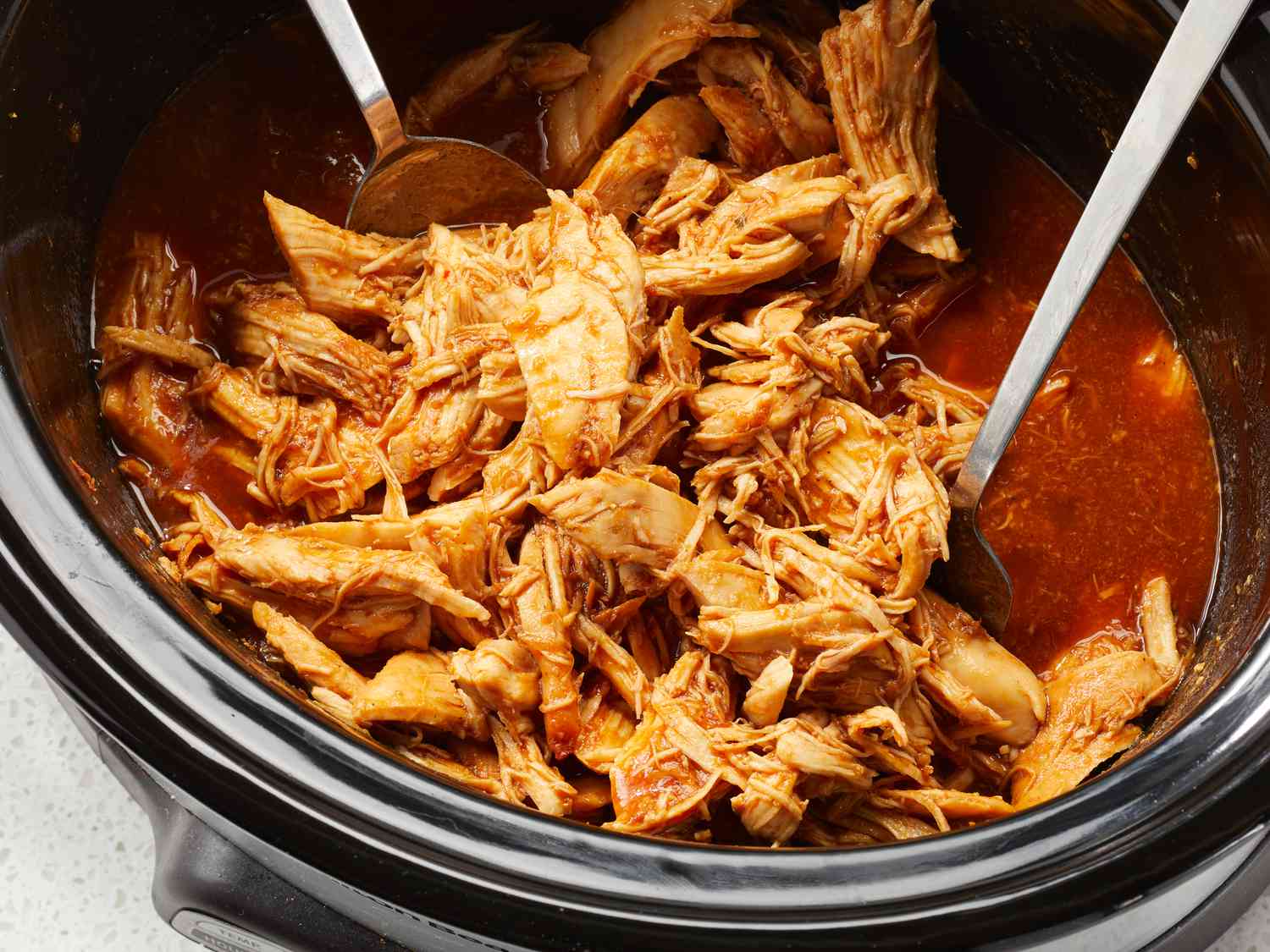 Chicken thighs in a slow cooker with sliced onions and a reddish citrus spice sauce being poured over the top
