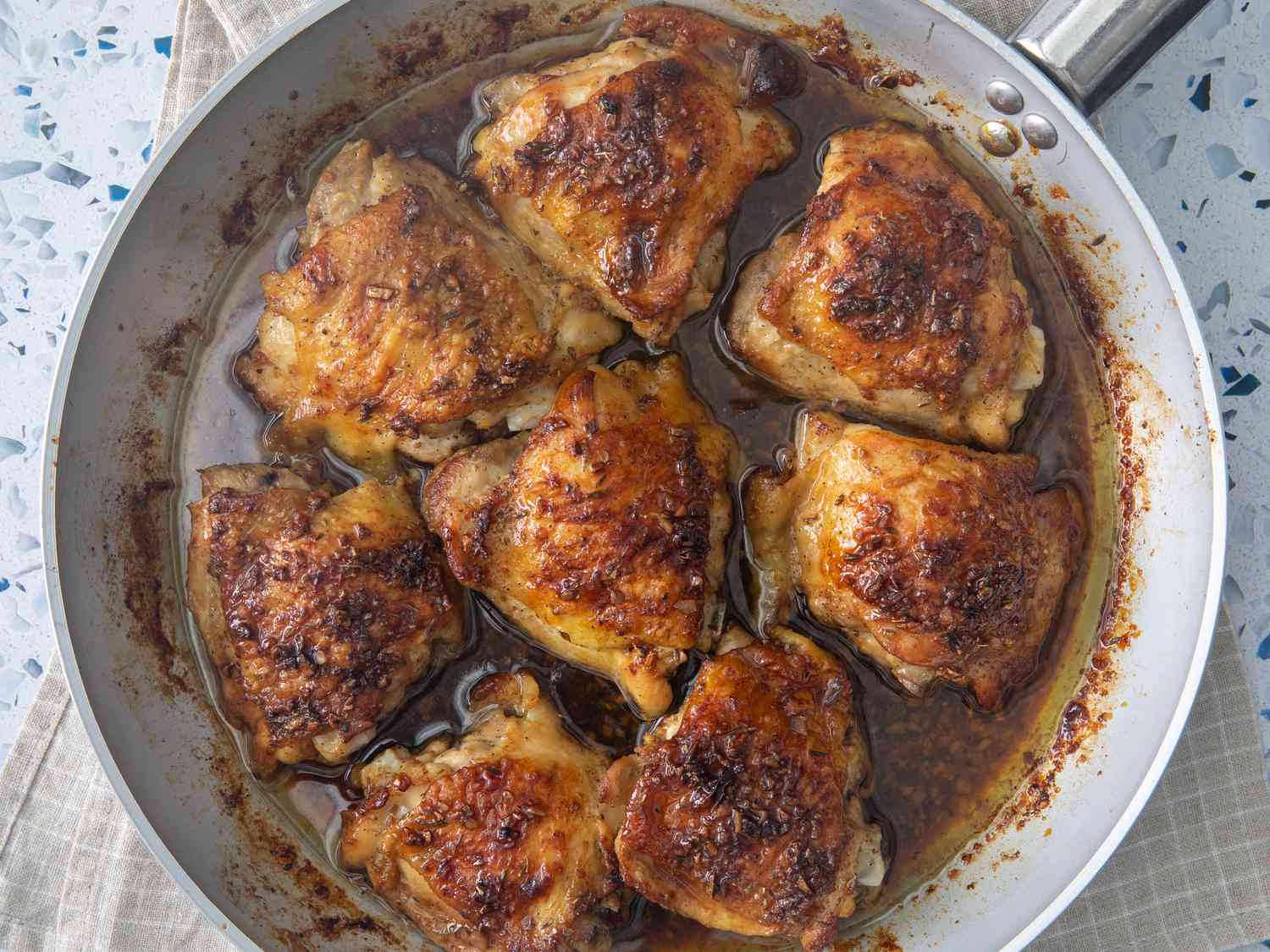 Chicken thighs searing skin-side down in a large skillet with lightly browned edges and rendered fat in the pan