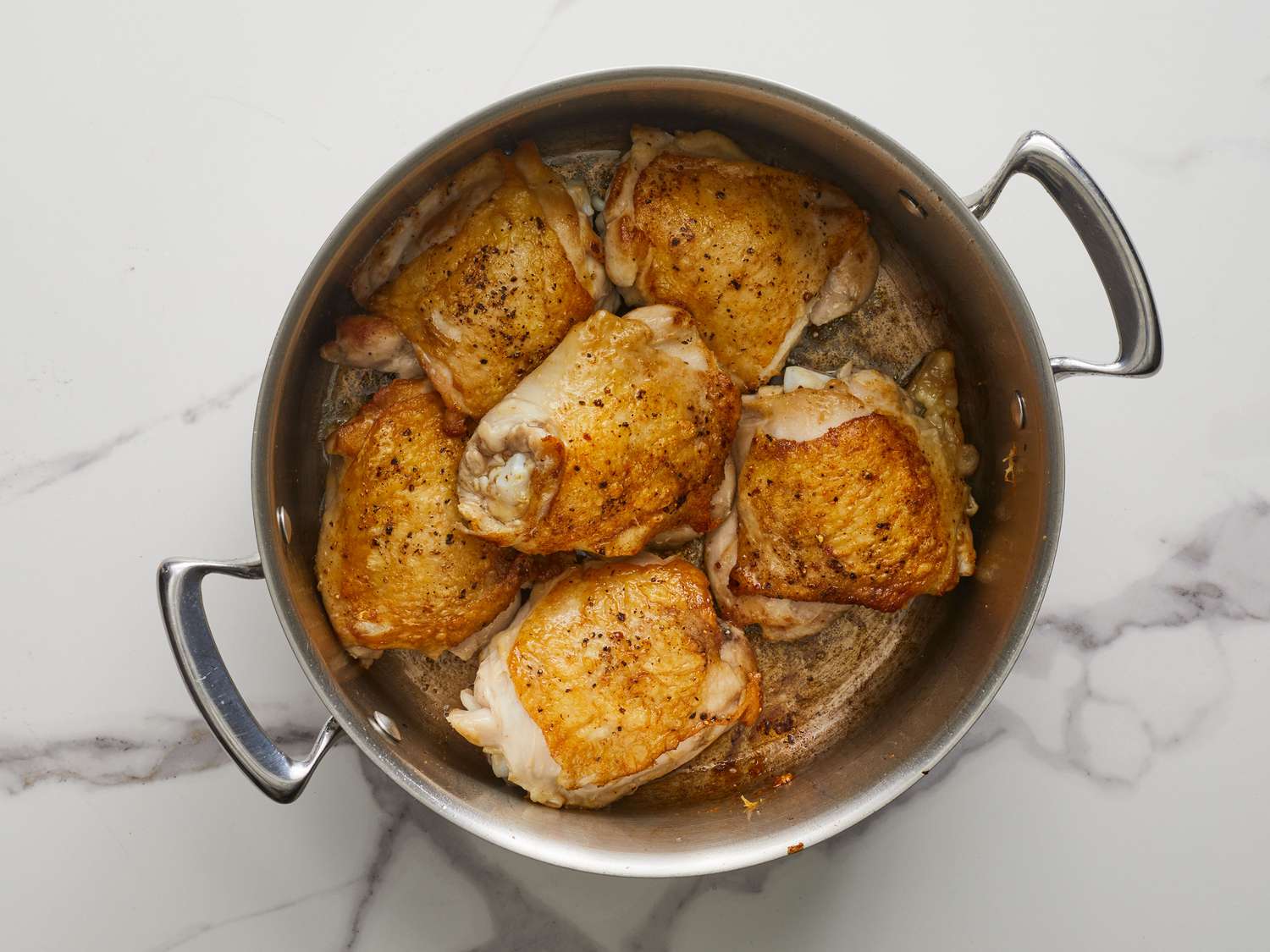 Chicken thighs simmering in a Dutch oven with broth, onion, and celery on a stovetop