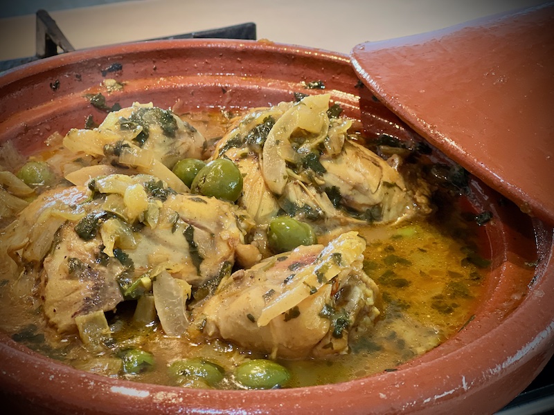 Chicken thighs simmering in a pot with chickpeas and apricots, sauce bubbling gently, a wooden spoon resting on the edge of the pot on a home stove