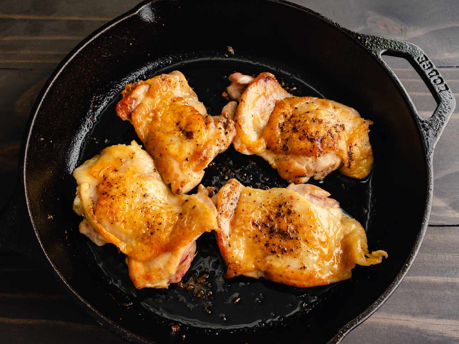 Chicken thighs sizzling skin-side down in a cast iron skillet on a stovetop as the skin turns golden and crisp
