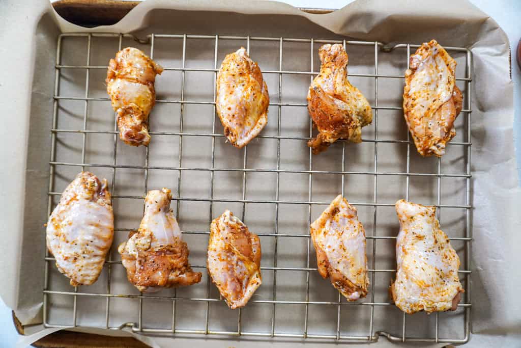 Chicken wings arranged in a single layer on a wire rack set over a rimmed baking sheet, ready to go into the oven, bright kitchen lighting, photorealistic