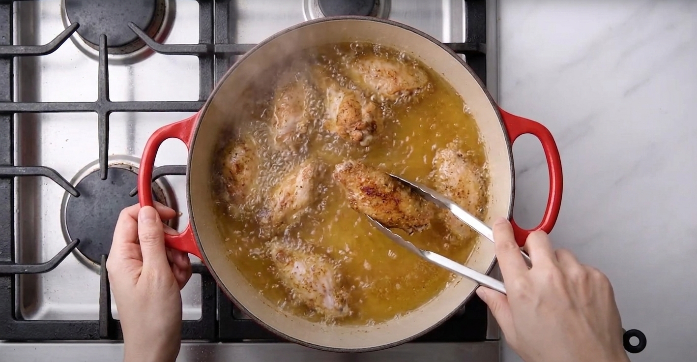 Chicken wings frying in bubbling oil inside a Dutch oven on a stovetop