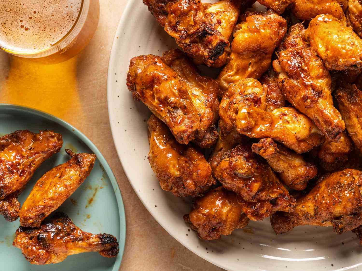 Chicken wings in a large bowl being tossed with a reddish dry rub, with a spoon and spice bowls nearby on a kitchen counter