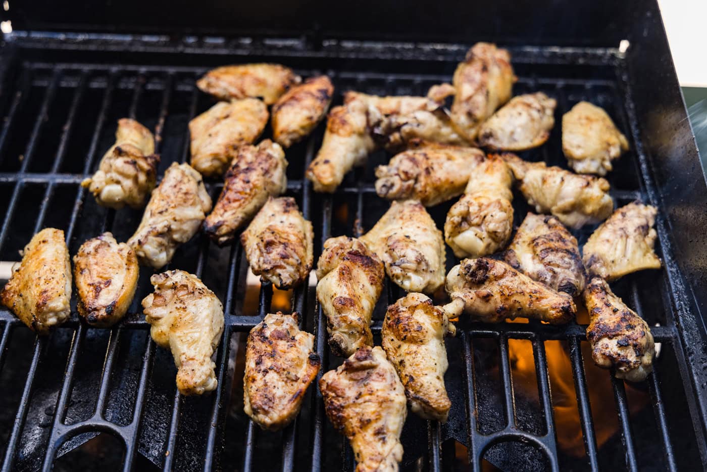 Chicken wings sizzling on grill grates with light char marks and rendered golden skin, photographed close up outdoors