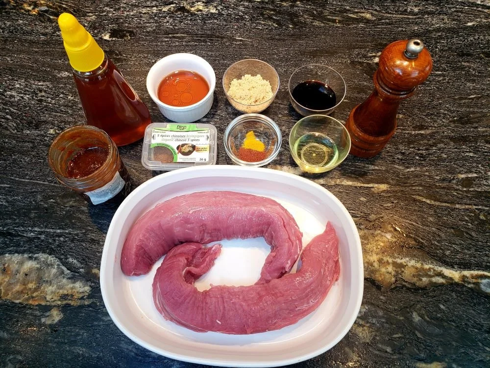 Chinese five spice and salt being rubbed onto a raw pork tenderloin on a cutting board in a home kitchen