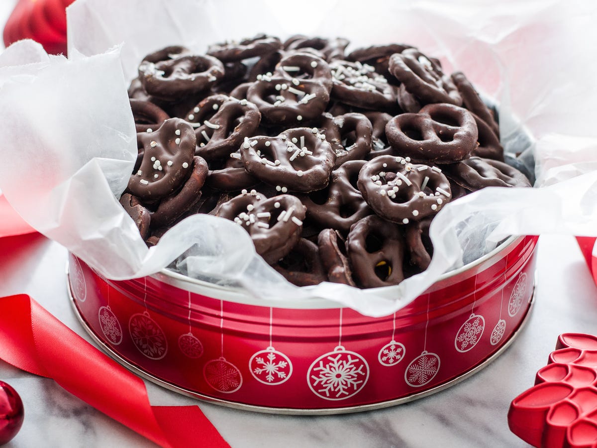 Chocolate covered pretzels stacked in an airtight container on a kitchen counter with parchment between layers