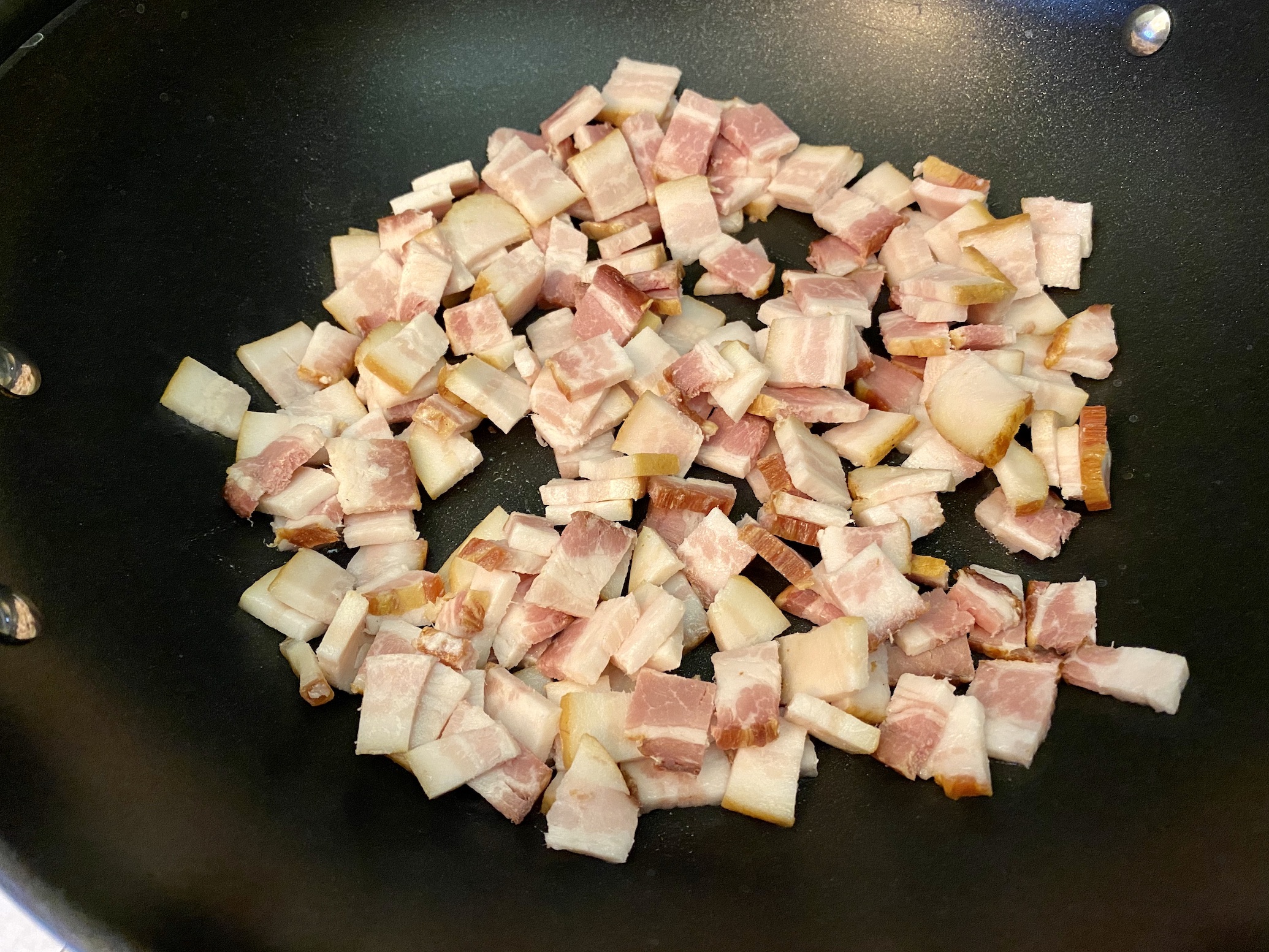 Chopped bacon and diced yellow onion prepped in small bowls on a kitchen counter next to trimmed green beans