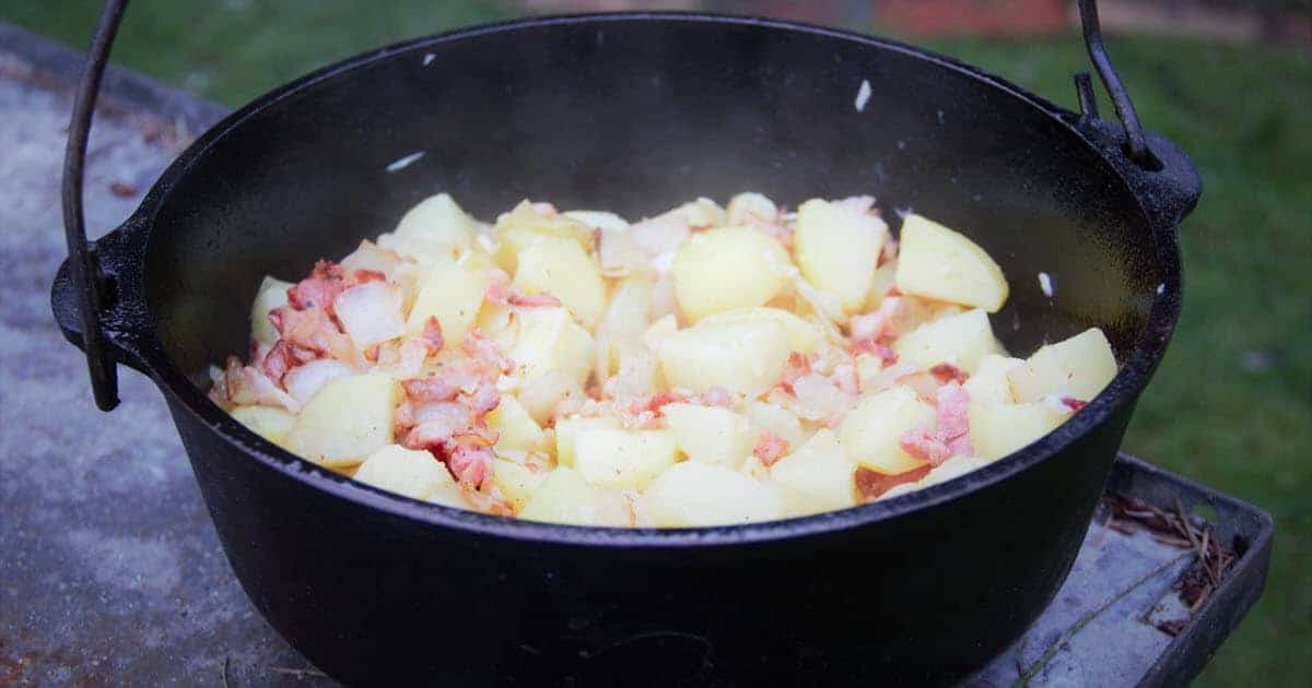 Chopped bacon sizzling in a Dutch oven on a stovetop with a wooden spoon stirring