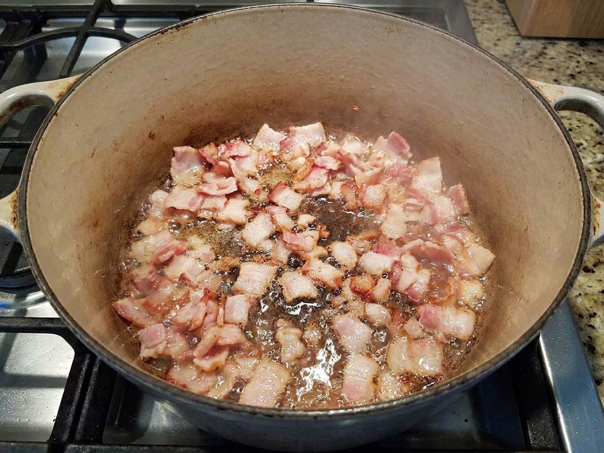 Chopped bacon sizzling in a Dutch oven on a stovetop, with fat rendering in the bottom of the pot