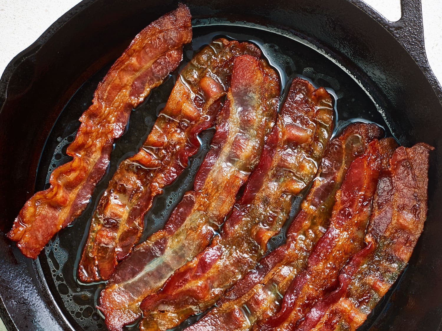 Chopped bacon sizzling in a cast iron skillet on a stovetop with rendered fat pooling lightly in the pan