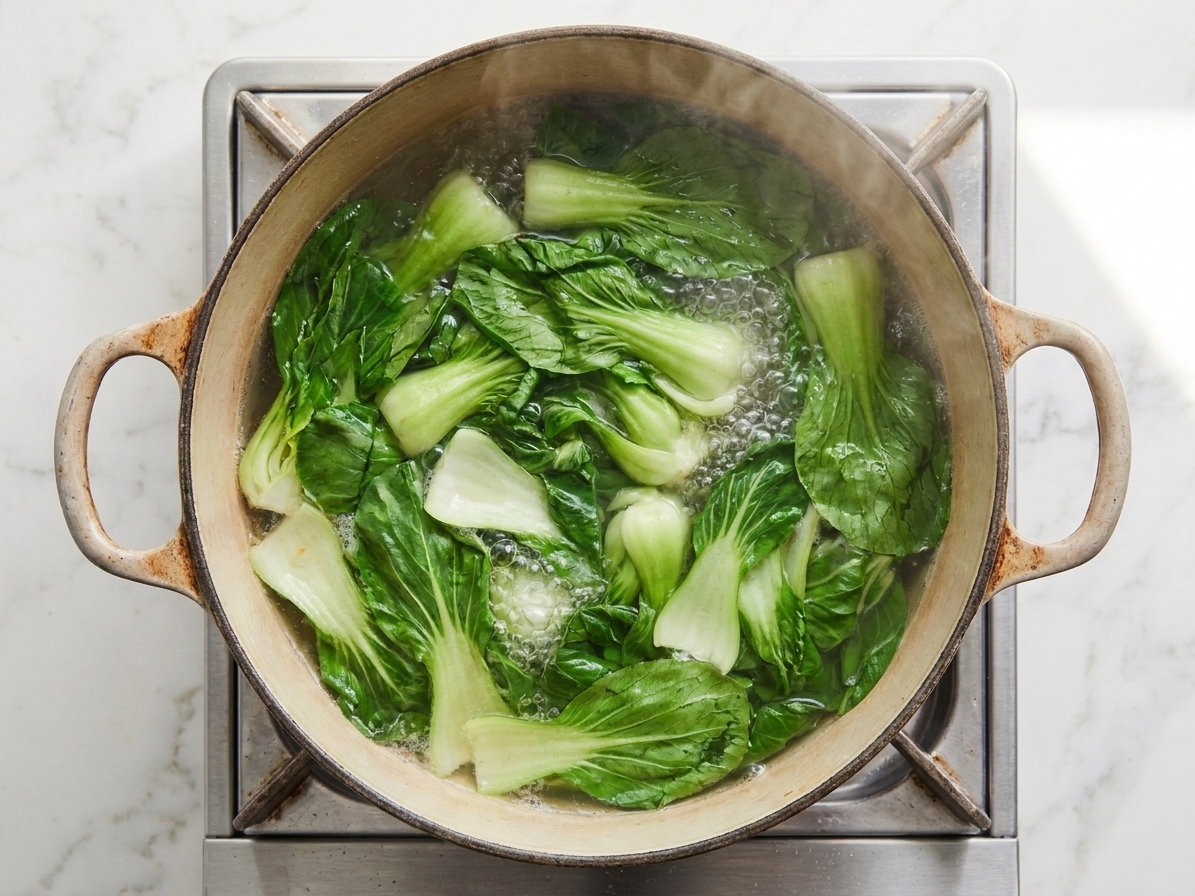 Chopped bok choy blanching in a pot of boiling water on a stovetop