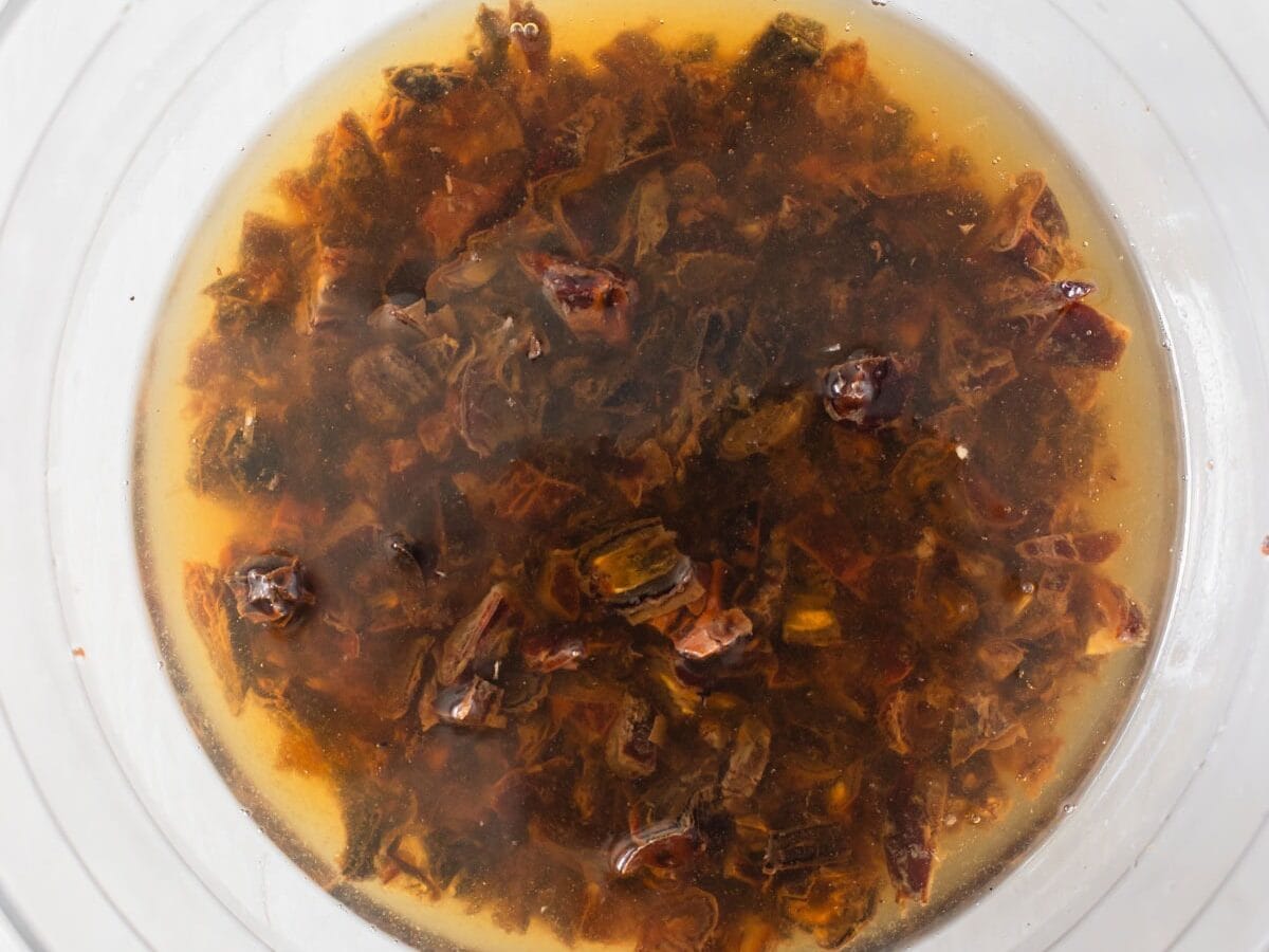 Chopped dates in a bowl being poured over with hot coffee, with a little steam rising on a kitchen countertop