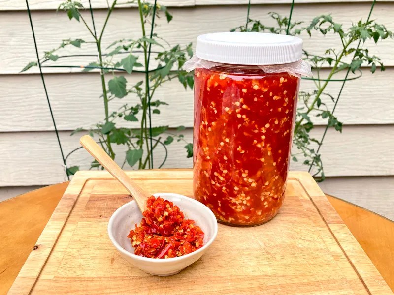 Chopped fresh chiles and peeled garlic cloves on a cutting board next to a glass jar, ready for fermenting
