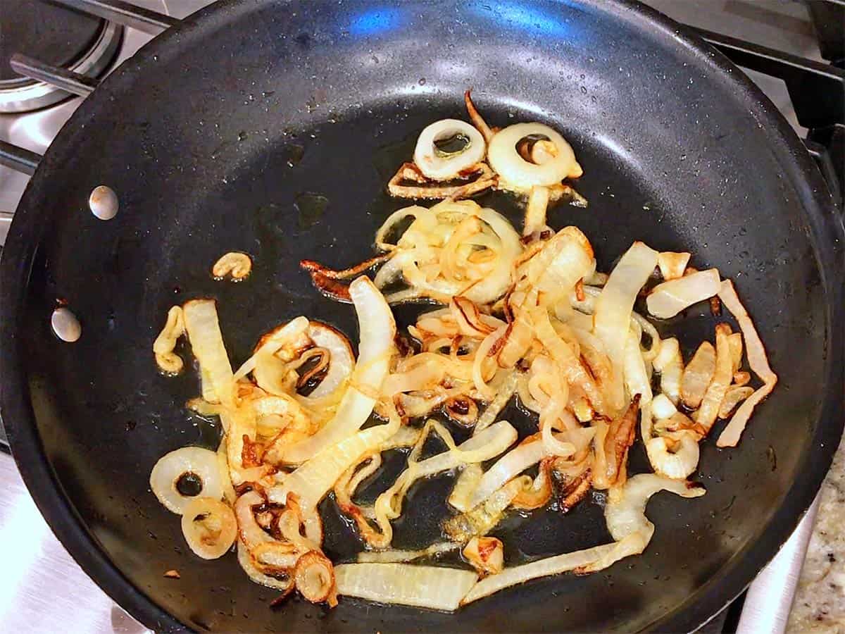 Chopped onion and minced garlic sizzling in a skillet with olive oil on a stovetop, with gentle steam rising as they soften