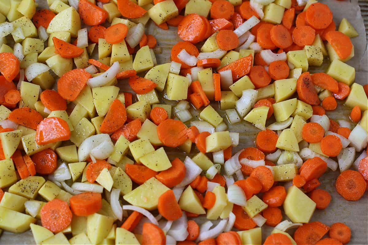 Chopped onion, carrot rounds, and potato chunks arranged on a cutting board on a tidy kitchen counter in warm light