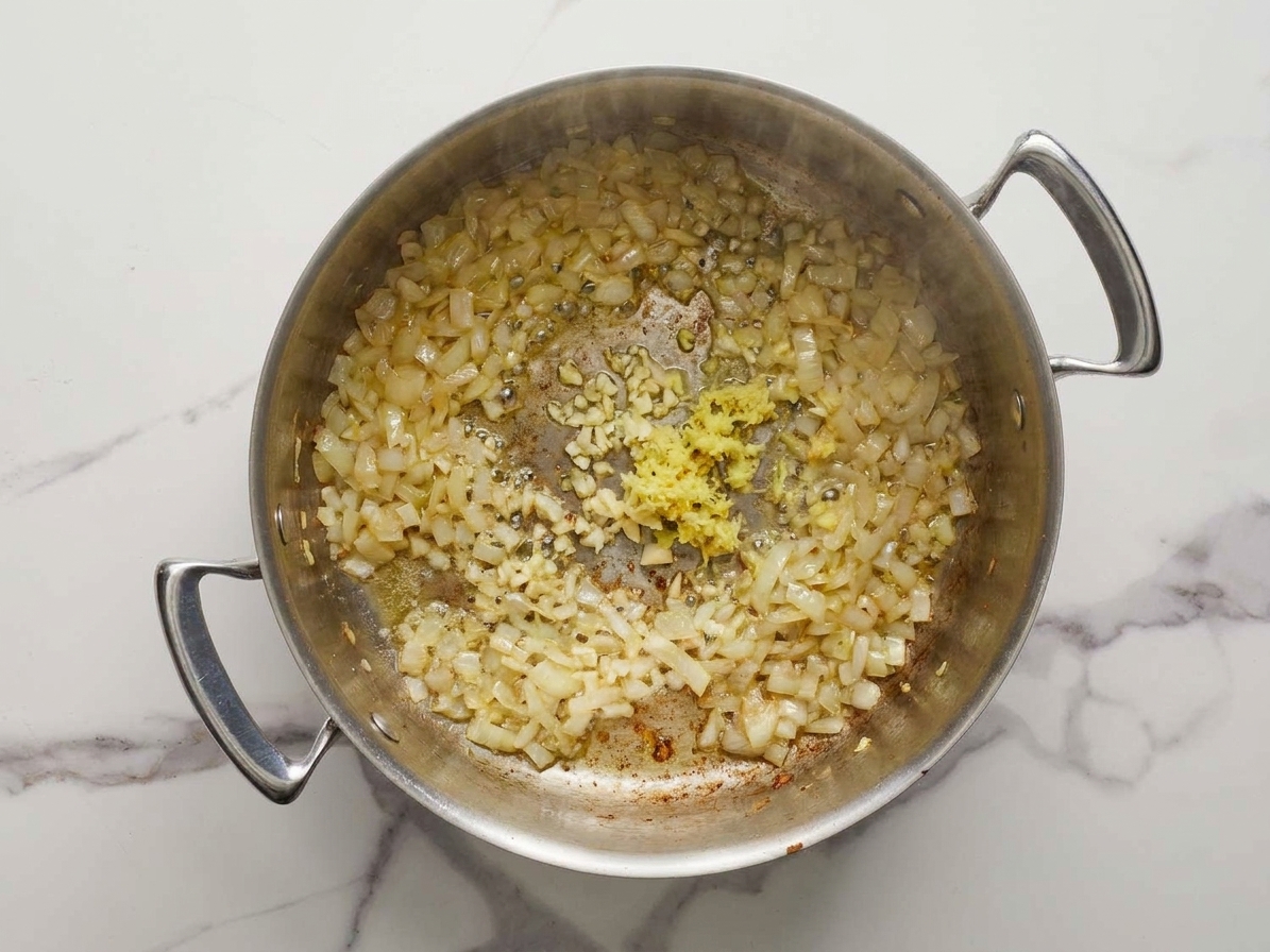 Chopped onion, minced garlic, and fresh ginger sizzling in a pot, glossy and fragrant as they soften