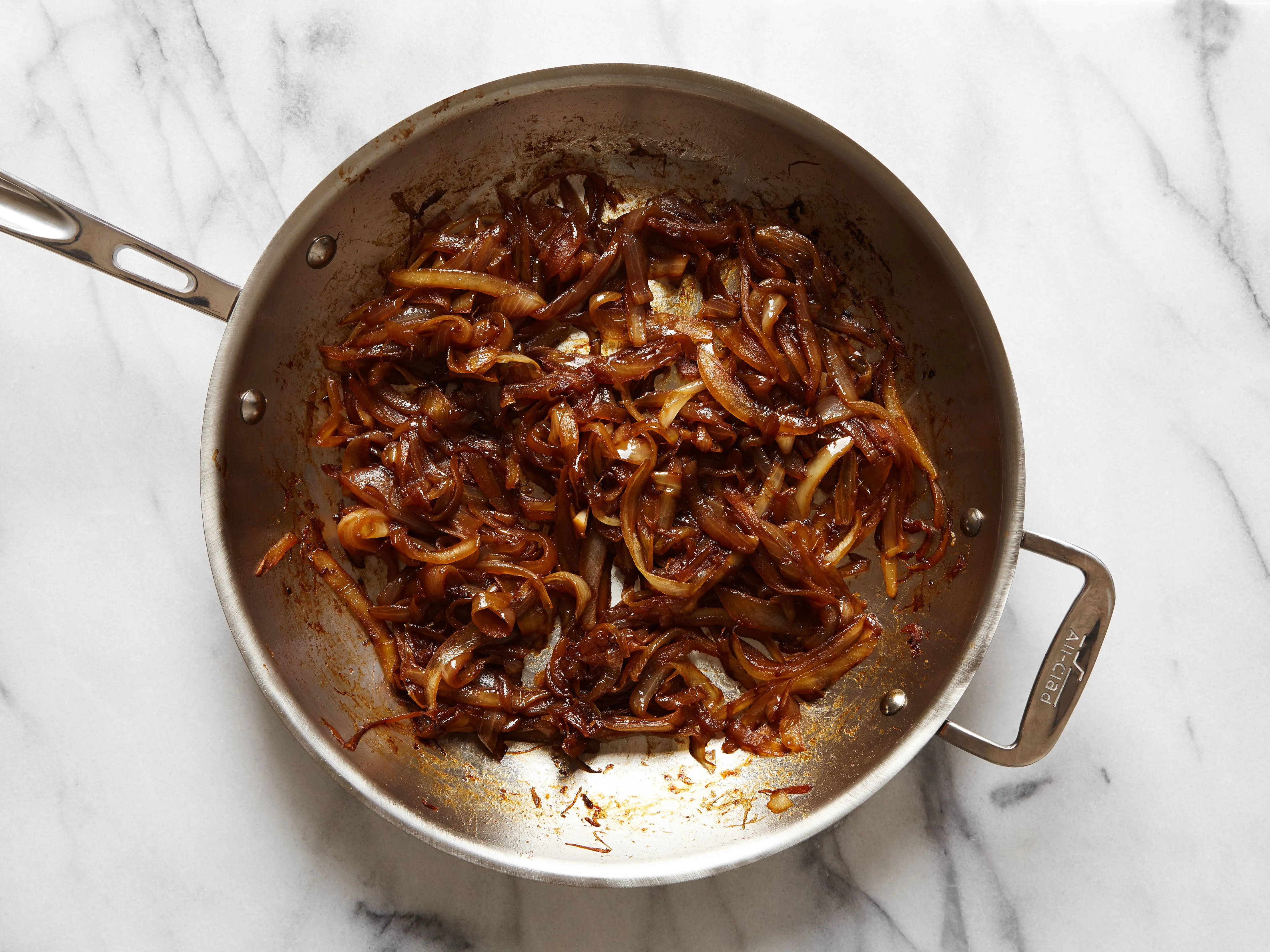 Chopped onions sautéing in butter in a stainless saucepan on a stovetop, with a wooden spoon stirring