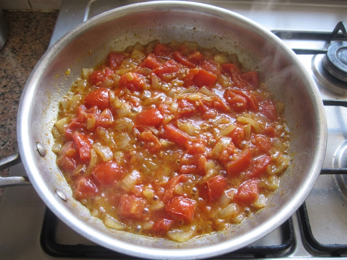 Chopped tomatoes and onions simmering in a skillet with butter, glossy and thickening as they cook