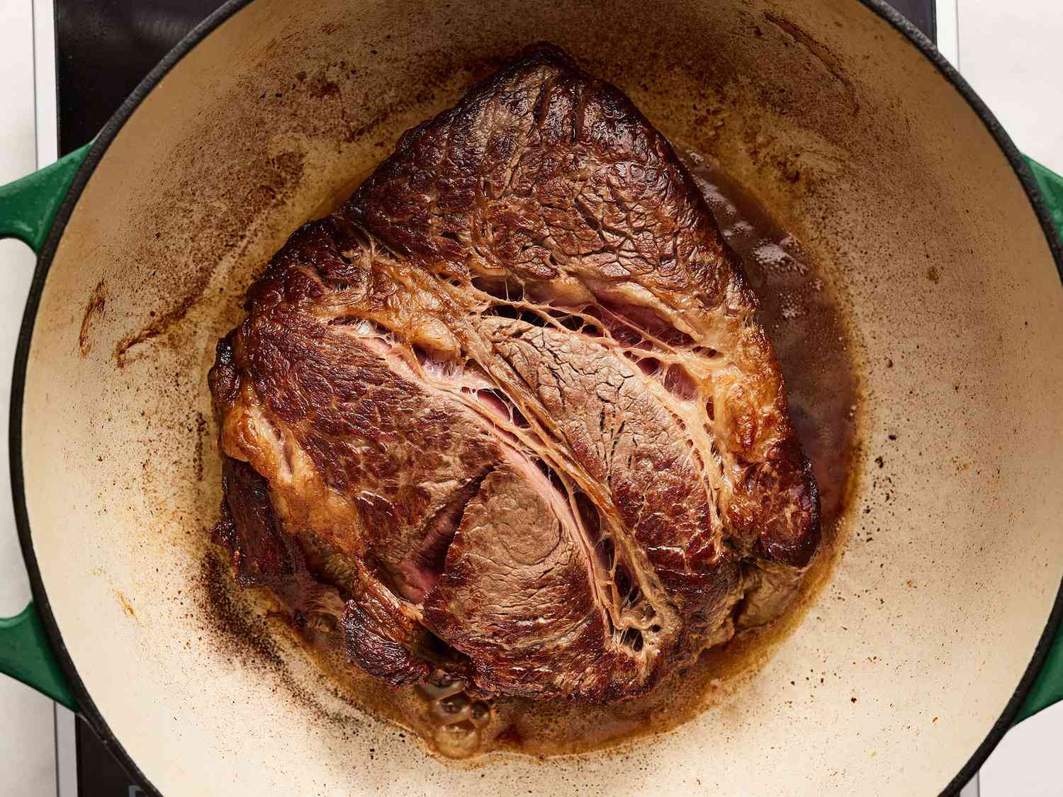 Chuck roast being seared in a heavy Dutch oven on a stovetop with a browned crust forming