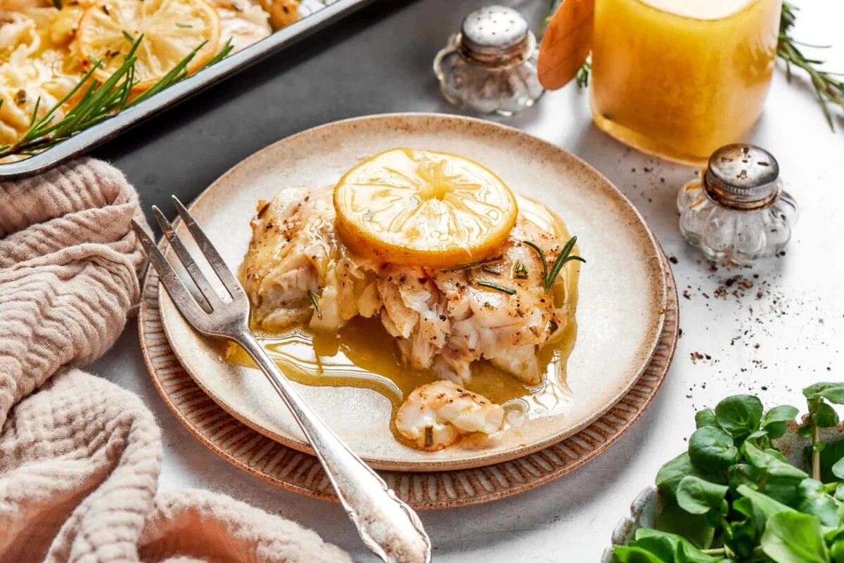 Close-up of a fork flaking a moist piece of baked halibut, showing tender white layers with a sheen of lemon butter