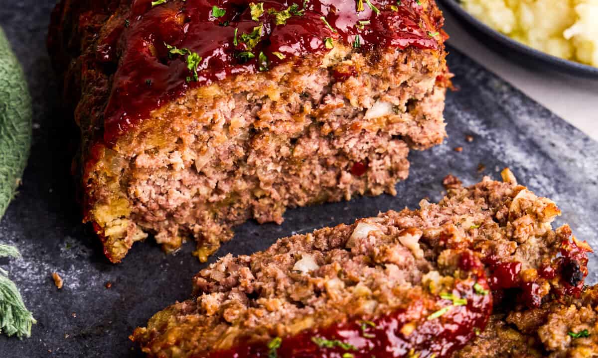 Close-up of a juicy slice of meatloaf showing a tender interior with small pieces of onion, on a plate with a bit of glaze, real food photography