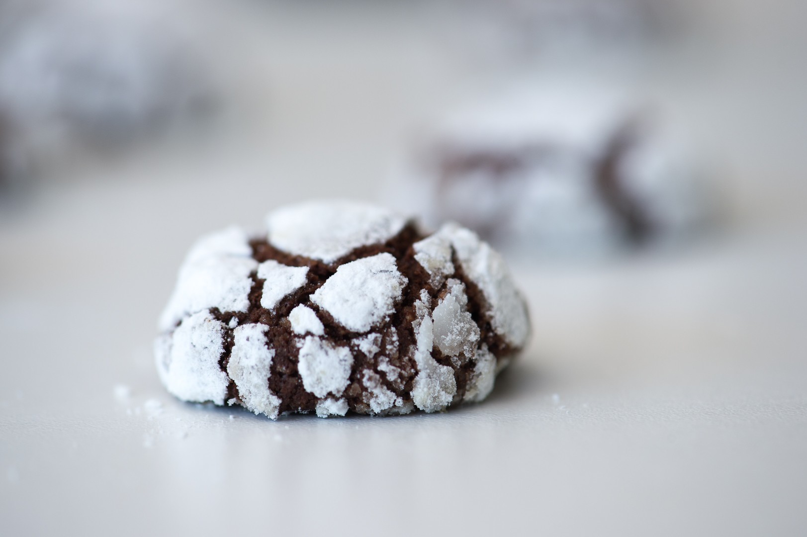 Close-up of a single chocolate crinkle cookie showing dramatic powdered sugar cracks and a slightly glossy fudgy center