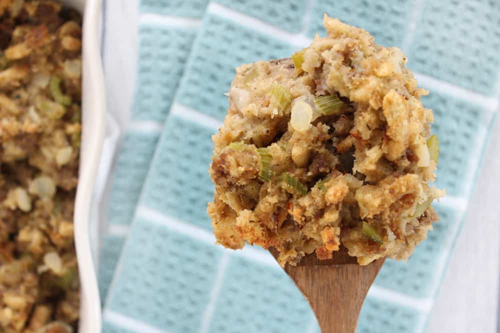 Close-up of a spoon scooping moist stuffing with browned bread cubes and visible celery pieces from a baking dish