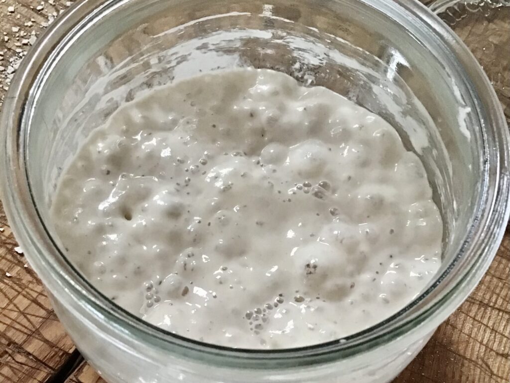Close-up of bubbly sourdough starter showing an airy honeycomb texture inside a glass jar on a kitchen counter