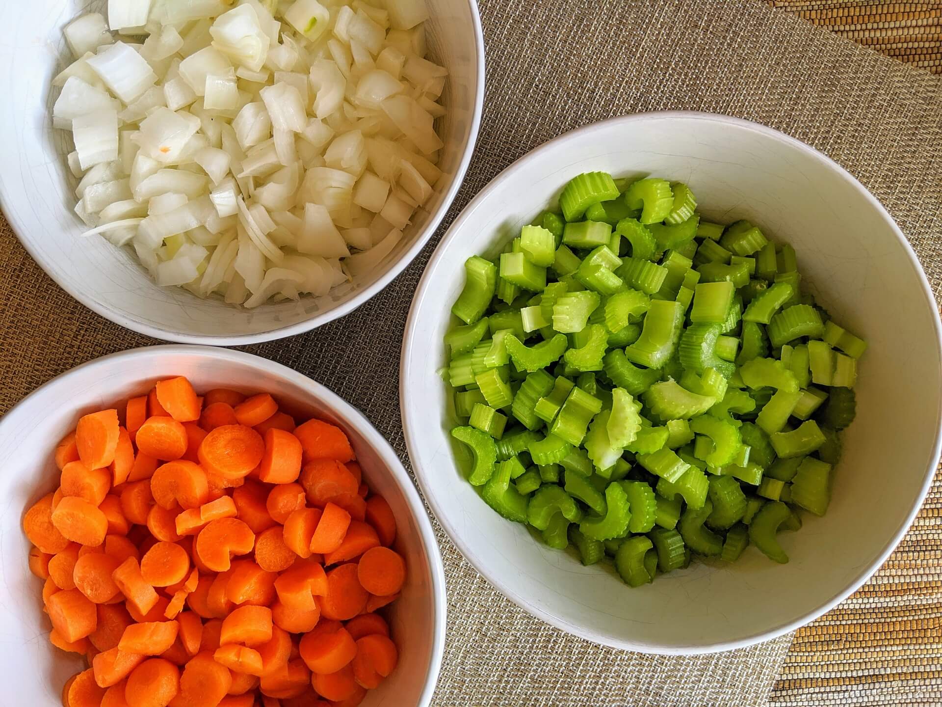 Close-up of chopped onion celery and green bell pepper piled on a cutting board beside minced garlic