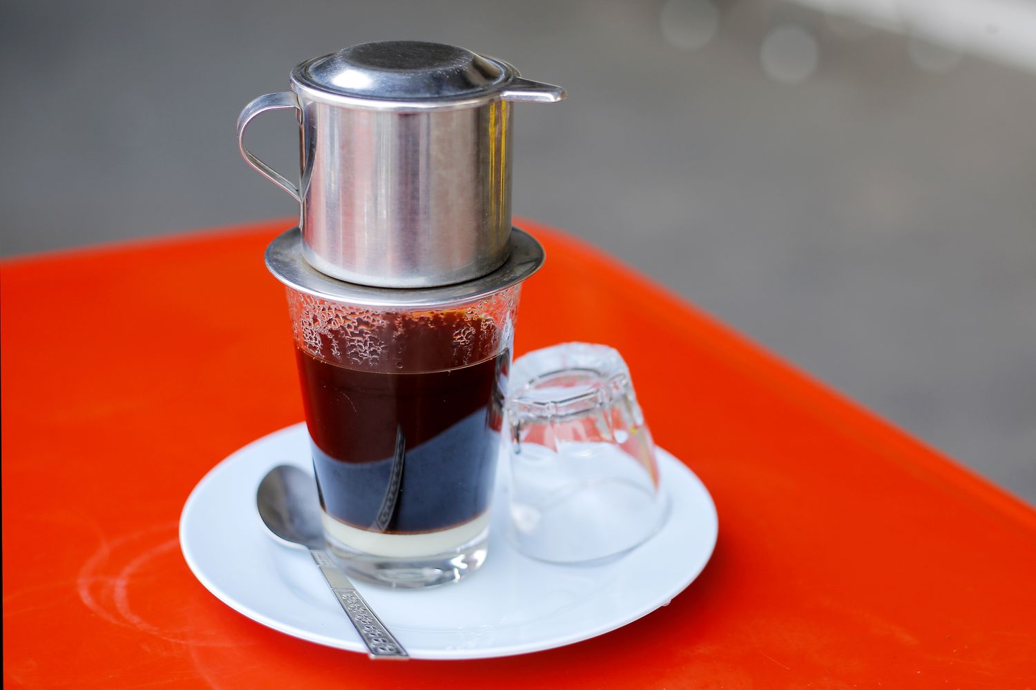 Close-up of coffee dripping through a stainless steel Vietnamese phin filter into a glass with condensed milk on a kitchen counter