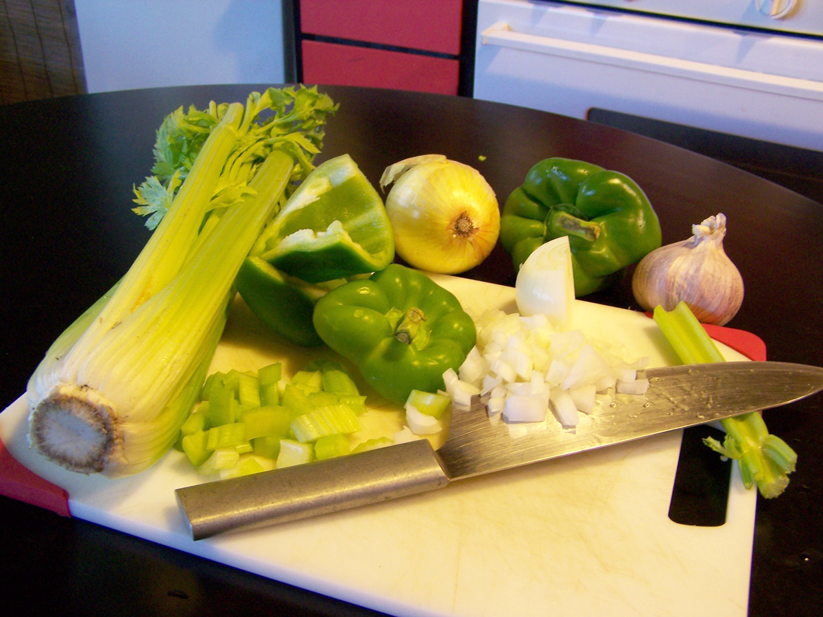 Close-up of diced onion, celery, and green bell pepper arranged in small bowls on a kitchen counter, ready for cooking