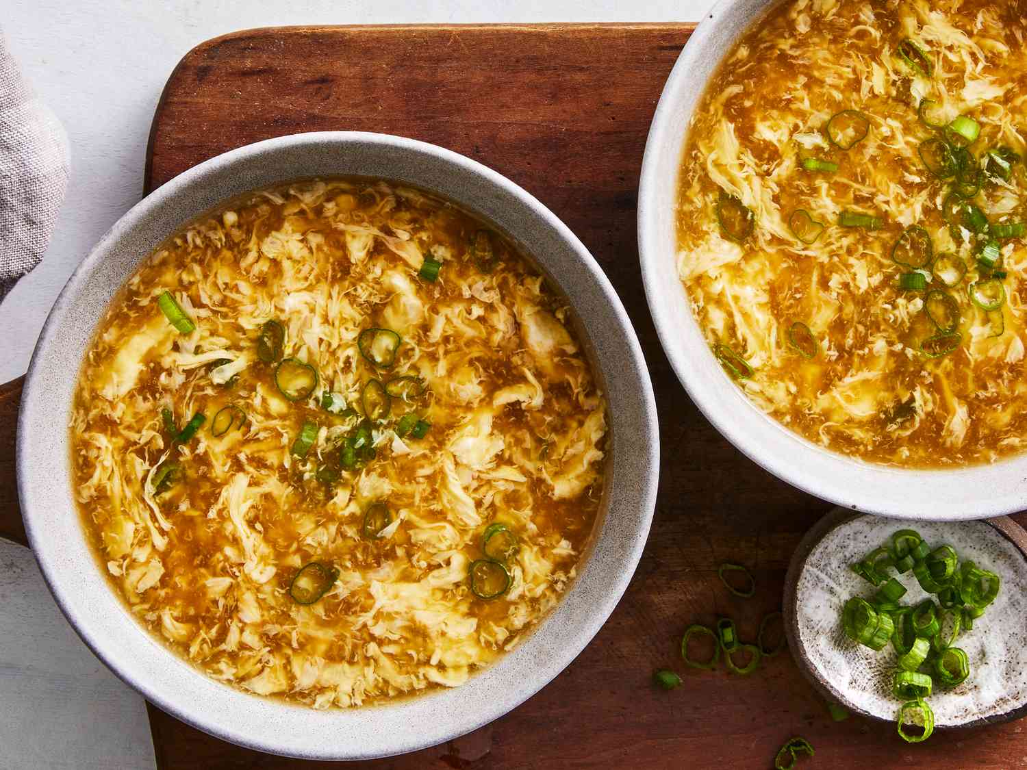 Close-up of egg drop soup in a bowl with delicate egg ribbons and fresh sliced scallions on top
