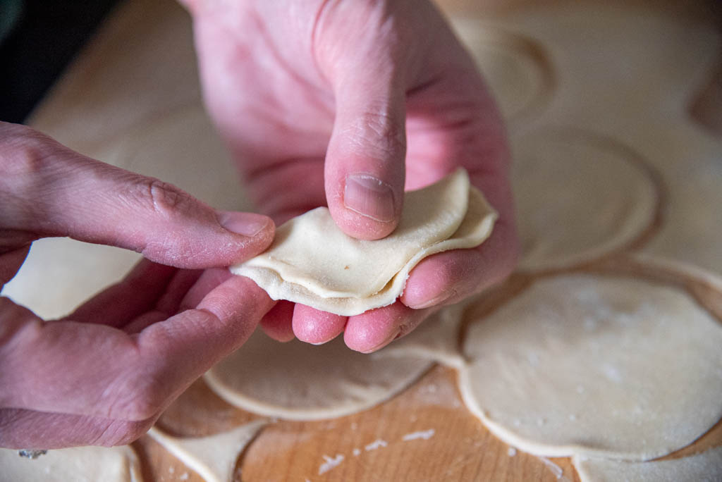Close-up of hands sealing a filled perogy by pinching the dough edges together on a floured wooden board