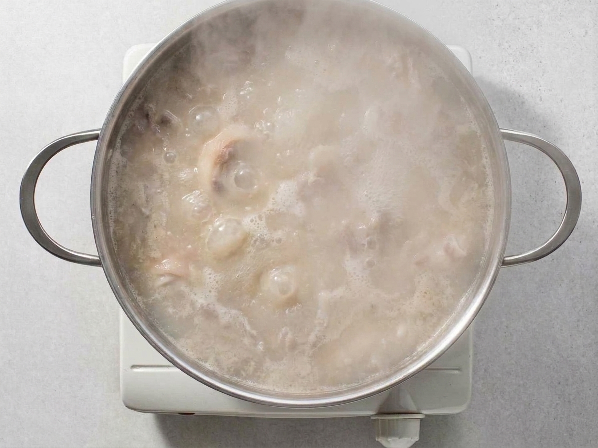 Cloudy tonkotsu broth boiling vigorously in a large stockpot on a stovetop with steam rising