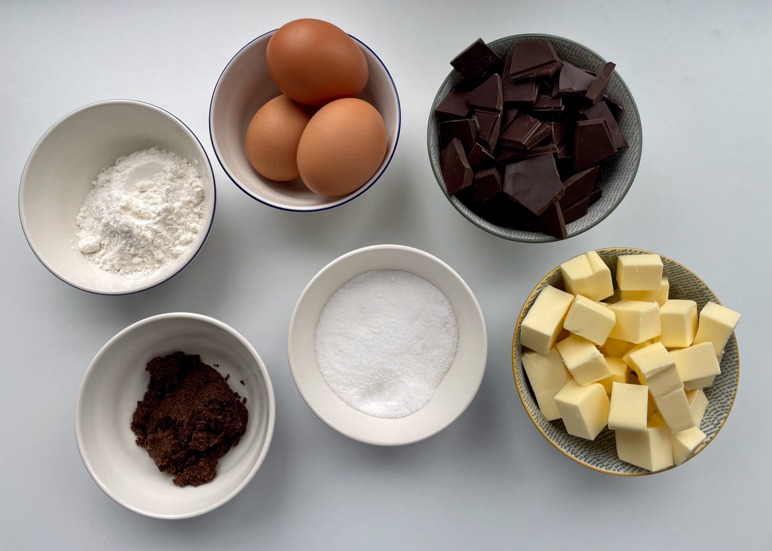 Cocoa powder, flour, sugars, eggs, and melted butter arranged on a kitchen counter for baking