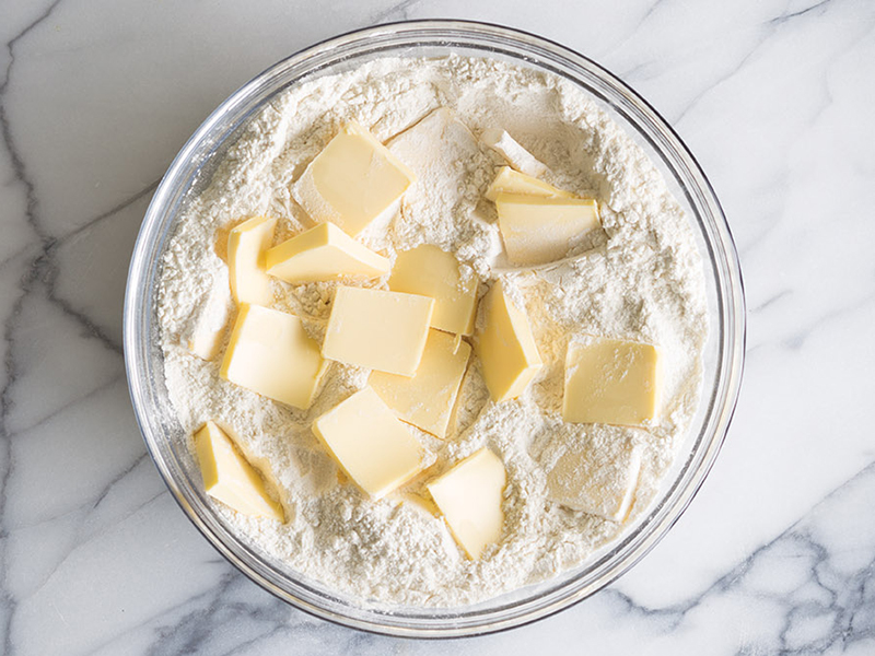 Cold butter being cut into flour with a pastry cutter in a large mixing bowl