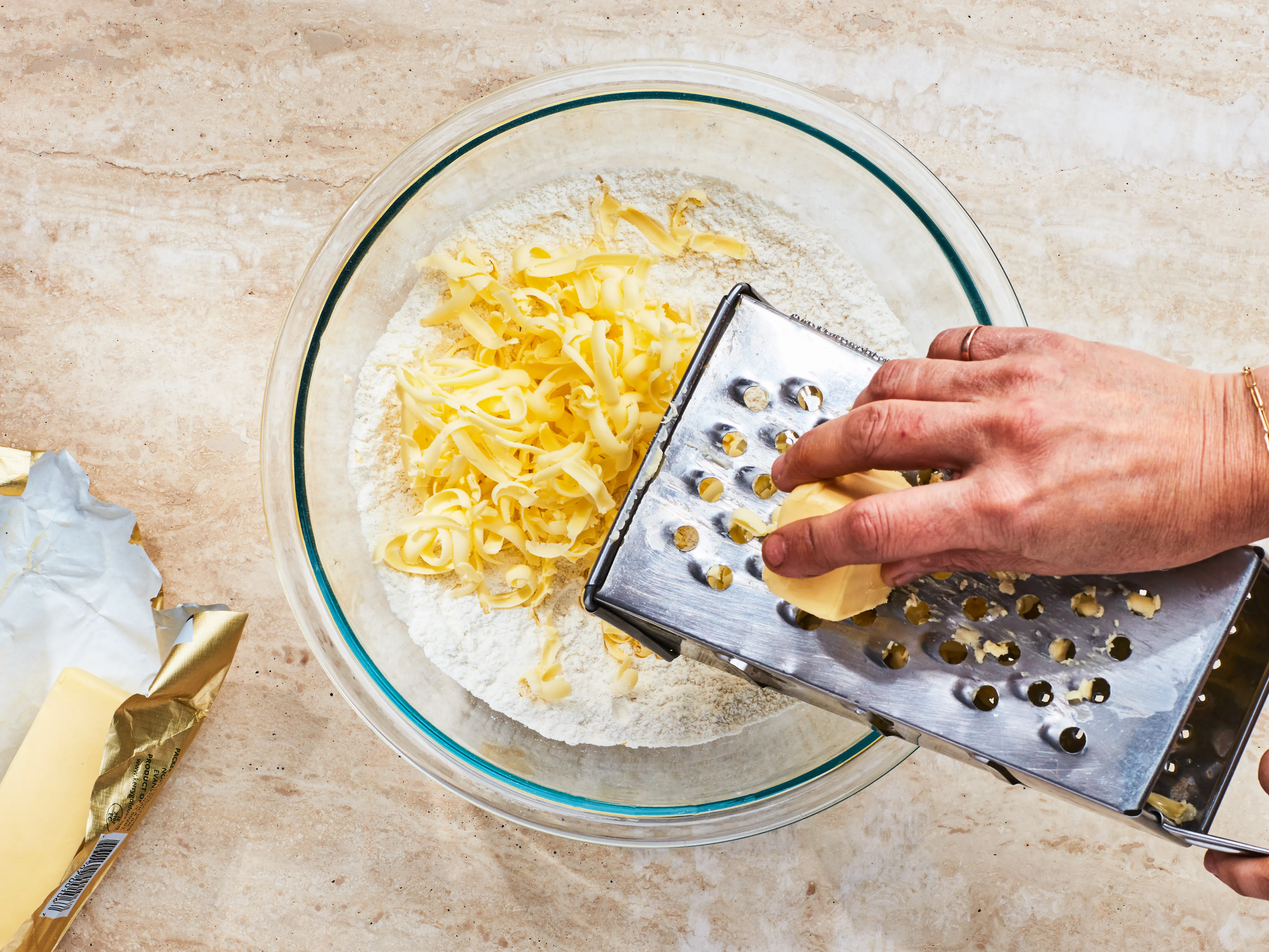 Cold butter being grated into a bowl of dry biscuit ingredients on a kitchen counter