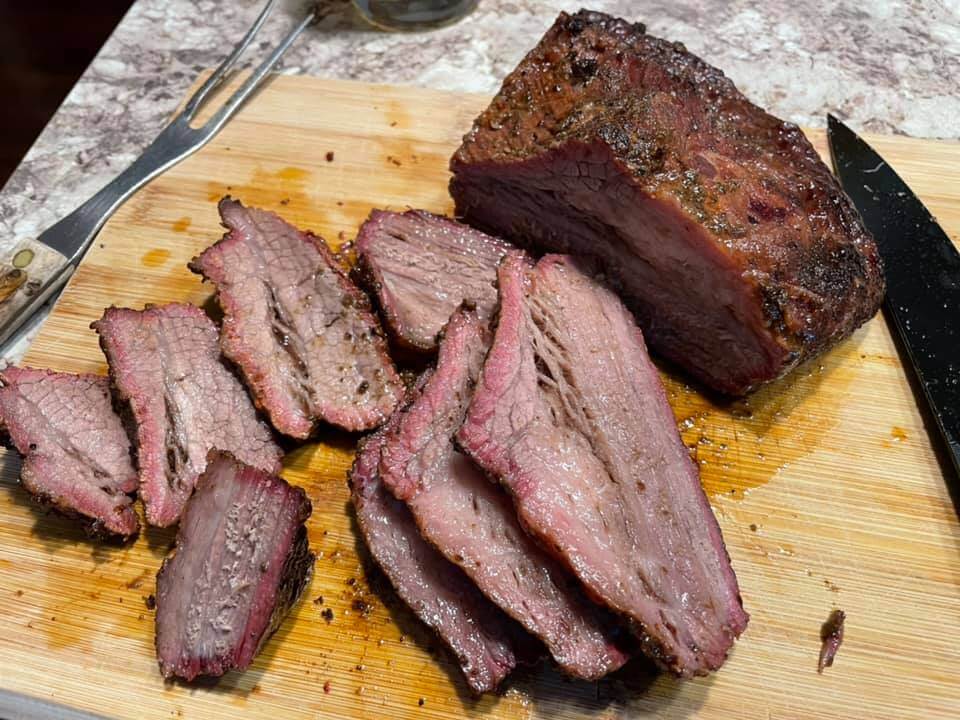 Container of sliced tri tip steak in the refrigerator next to a small container of sauce on a clean kitchen shelf