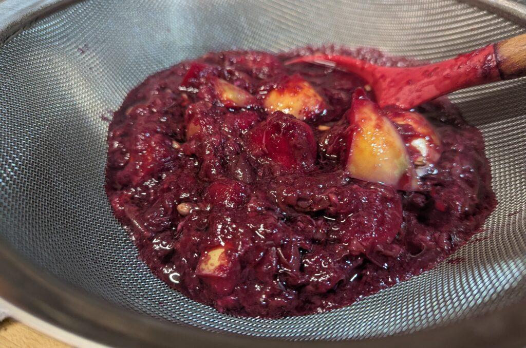 Cooked apples draining in a cloth jelly bag suspended over a bowl on a kitchen counter, clear apple juice collecting below