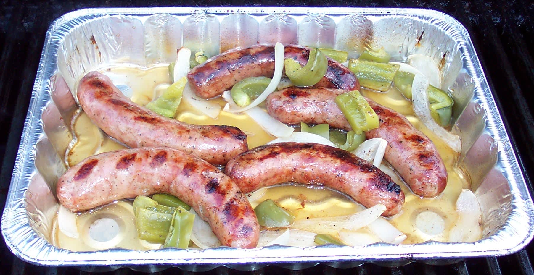 Cooked beer brats and onions packed in a glass meal prep container on a kitchen counter