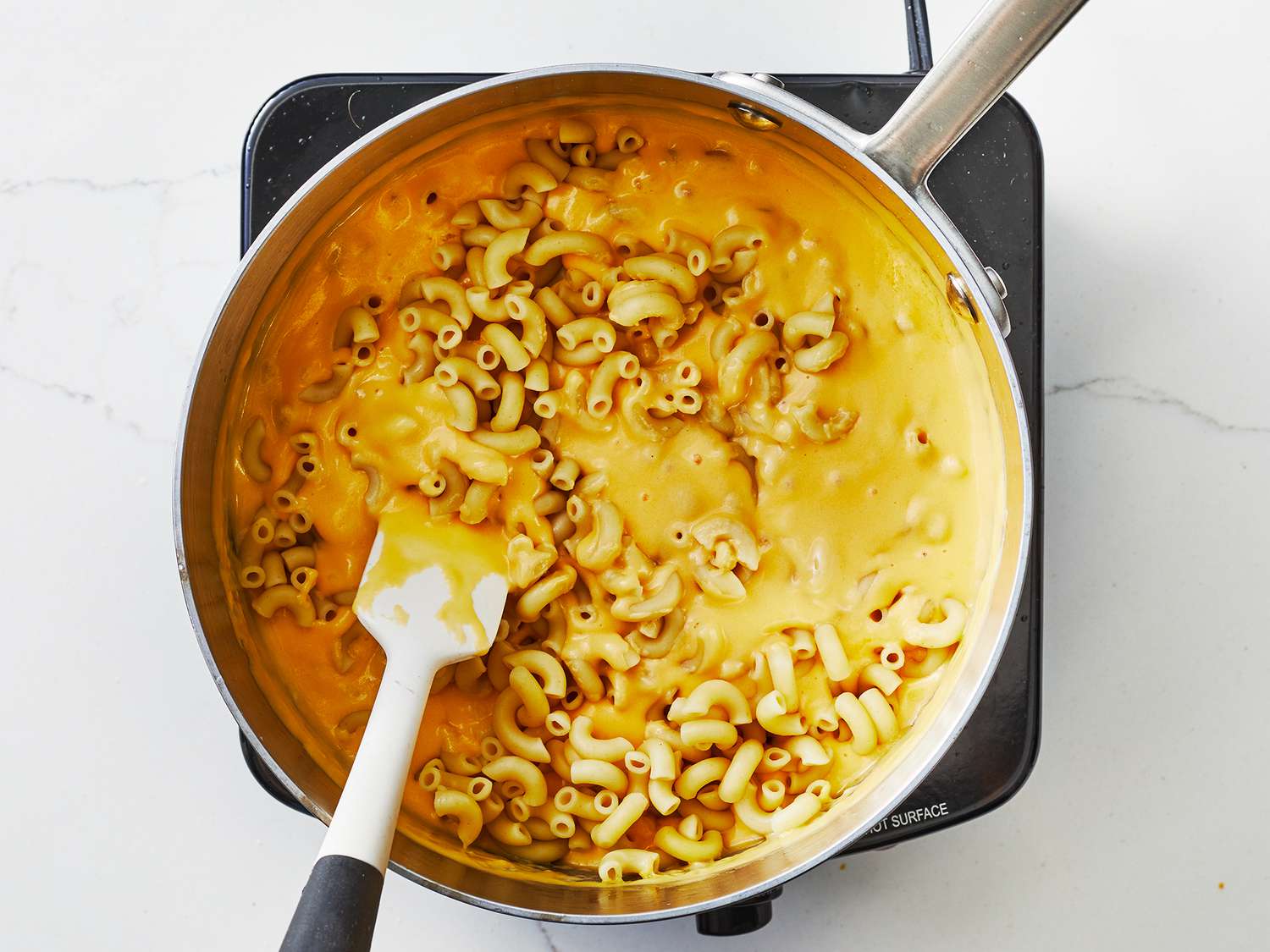 Cooked elbow macaroni being folded into a pot of creamy cheese sauce with a wooden spoon on a stovetop