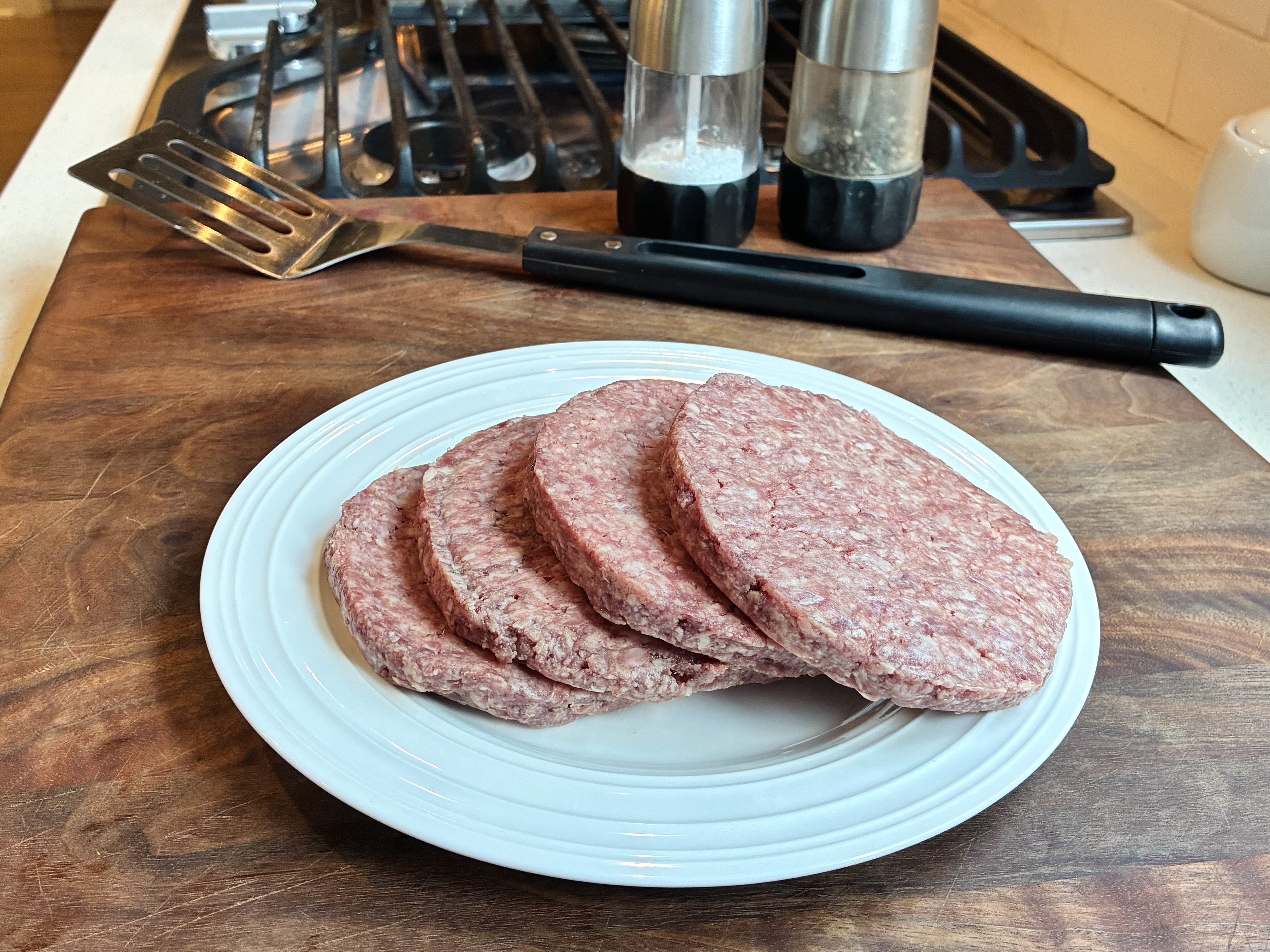 Cooked hamburger patties resting in a glass meal prep container with parchment between layers on a kitchen counter