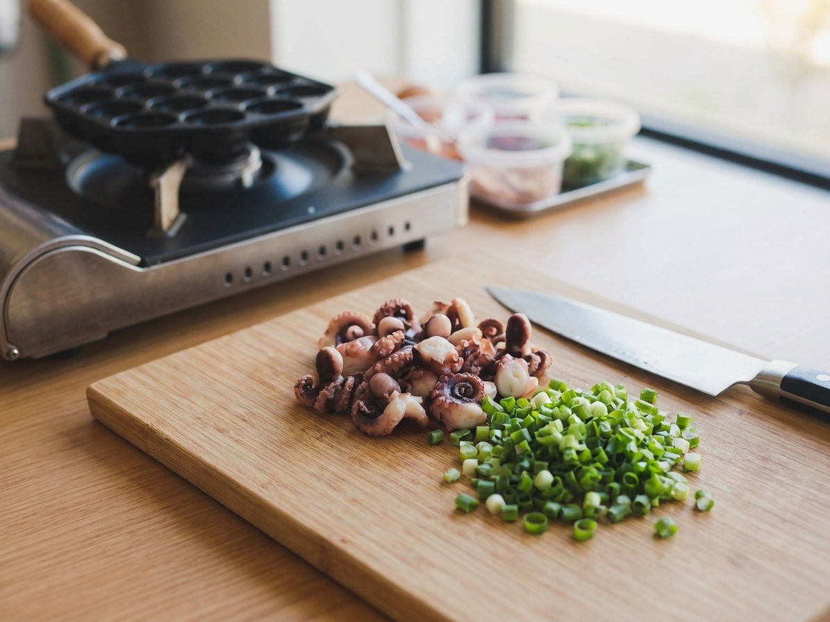 Cooked octopus cut into small pieces on a cutting board with a knife and green onions nearby