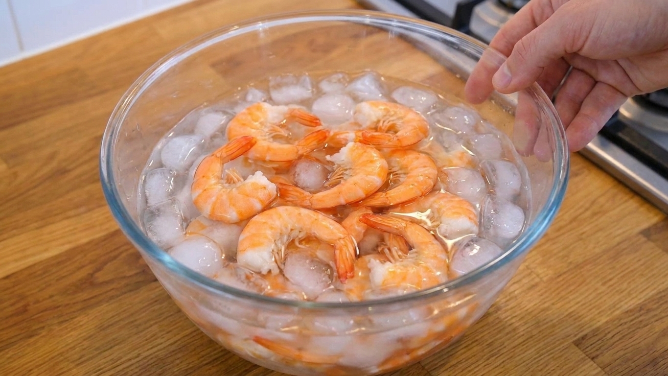 Cooked shrimp cooling in a large bowl of ice water on a kitchen counter