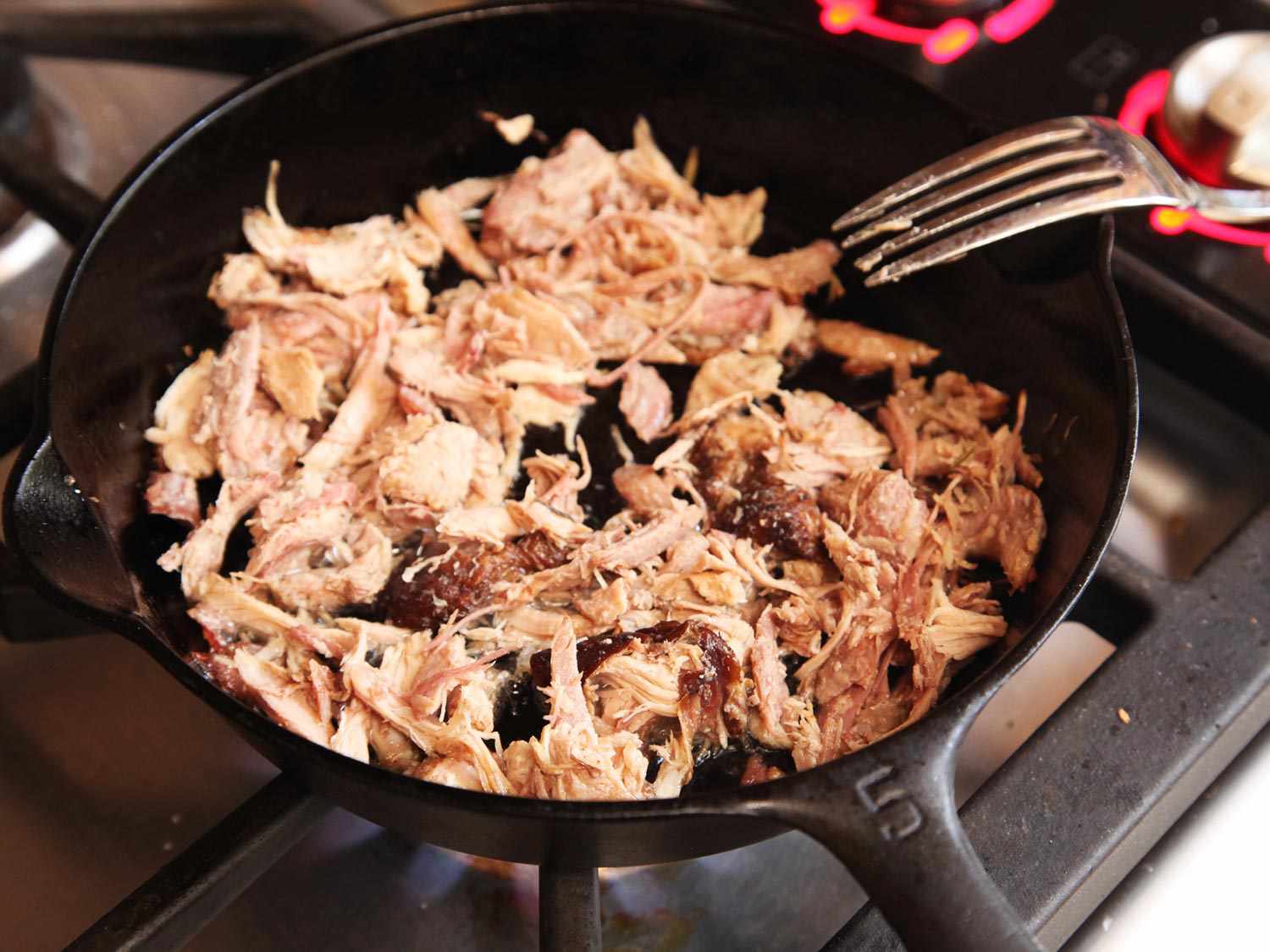 Cooked turkey being chopped into bite-size pieces on a wooden cutting board with a chef's knife