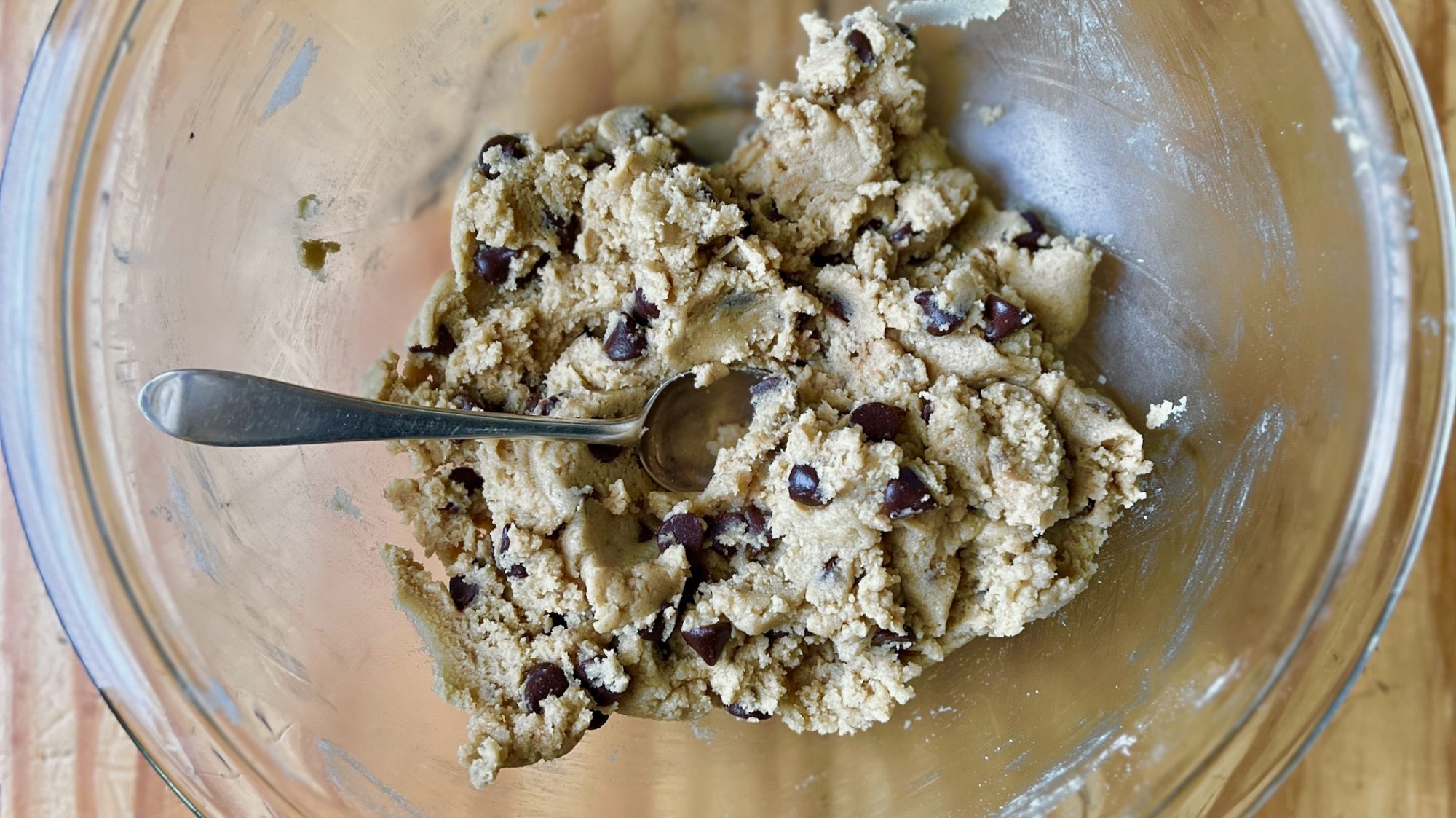 Cookie dough being mixed in a stainless steel bowl with a spatula, showing chocolate chips folded throughout on a bright kitchen counter
