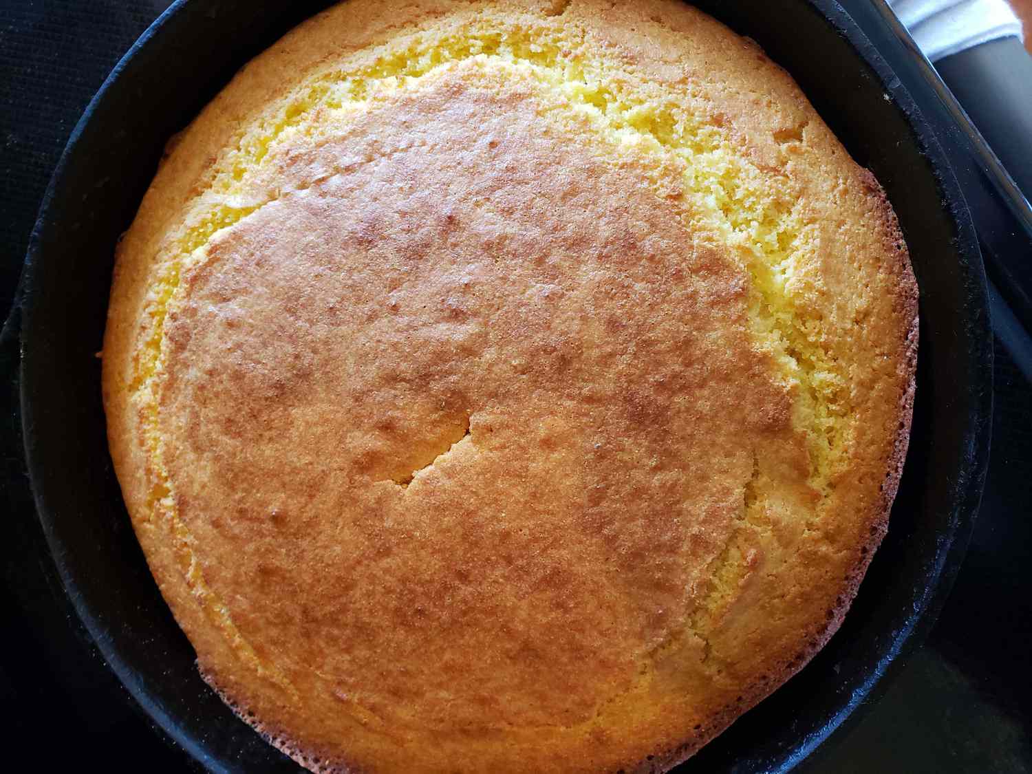 Cornbread batter being poured into a hot buttered cast iron skillet with visible sizzling bubbles around the edges