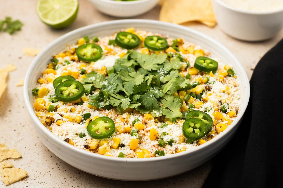 Cotija cheese, halved limes, fresh cilantro, and a diced jalapeno on a cutting board on a kitchen counter